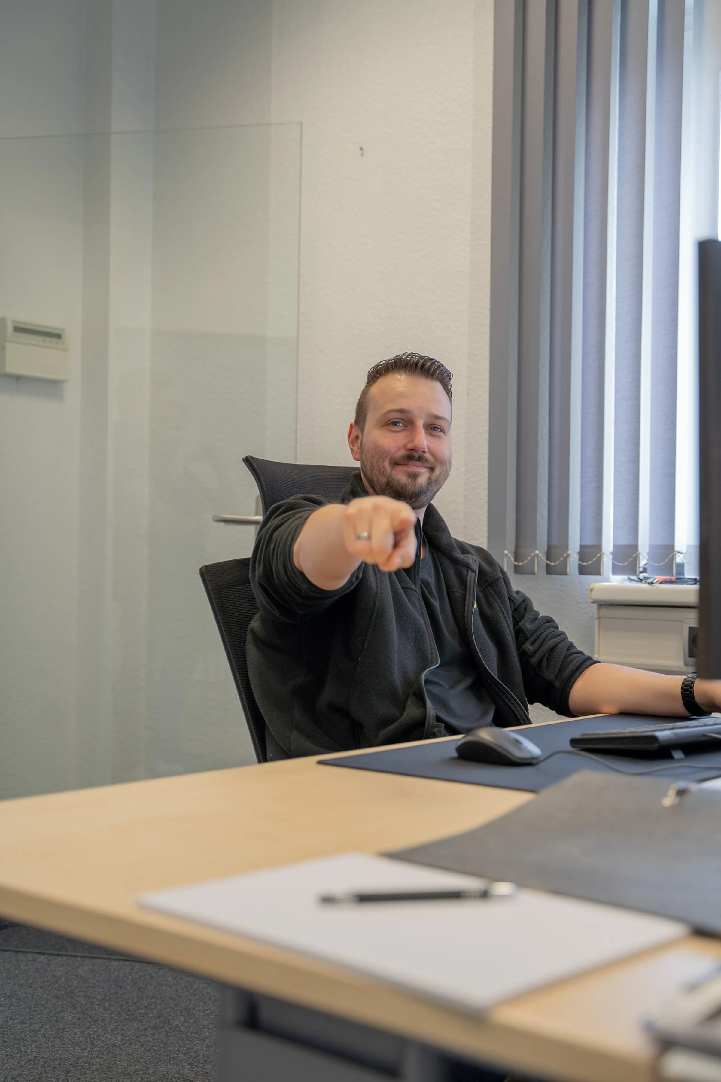Lächelnder Mitarbeiter im Büro zeigt in die Kamera