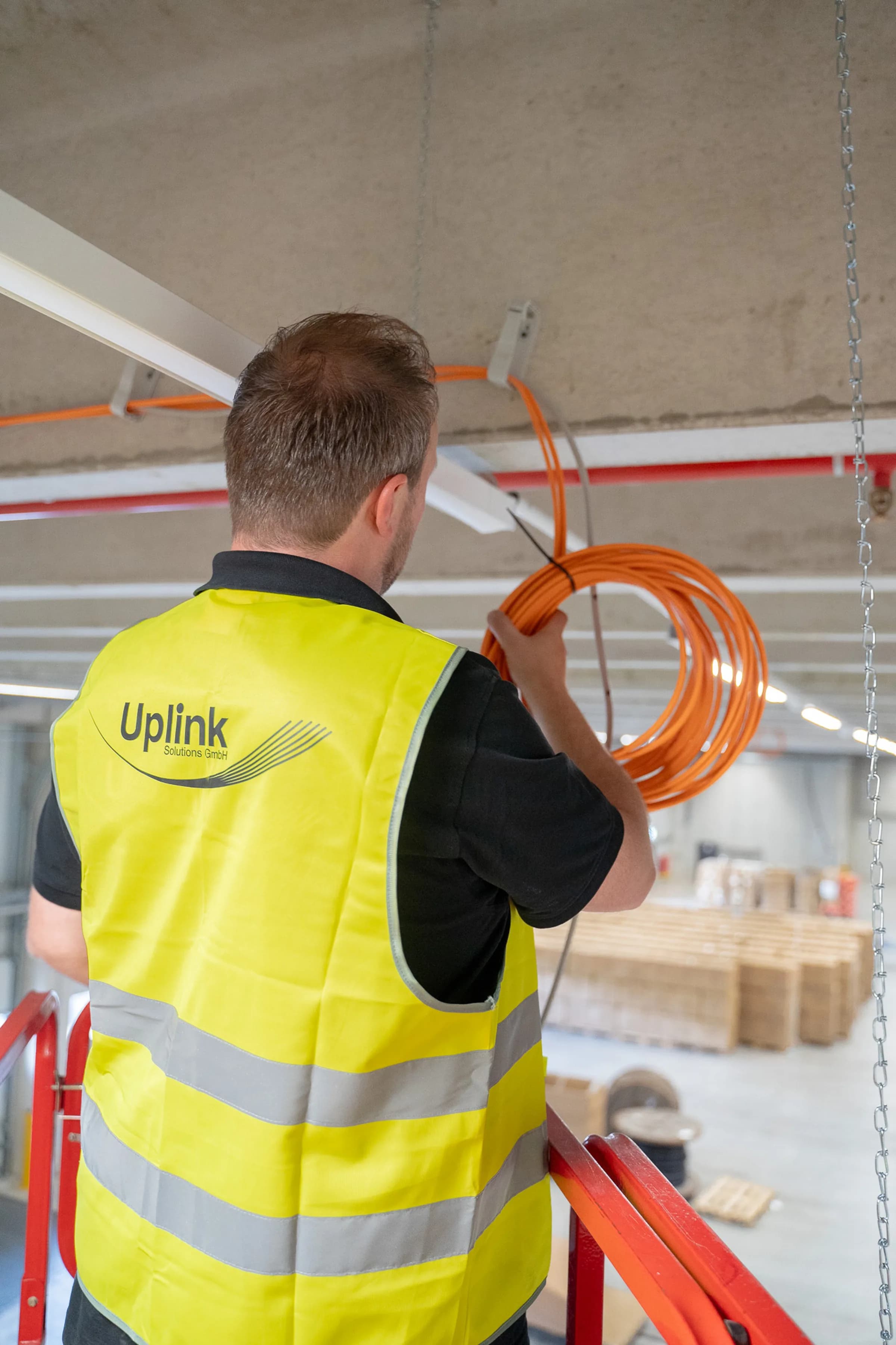 Uplink-Techniker in Warnweste mit orangefarbenem Kabel bei Arbeiten an der Decke