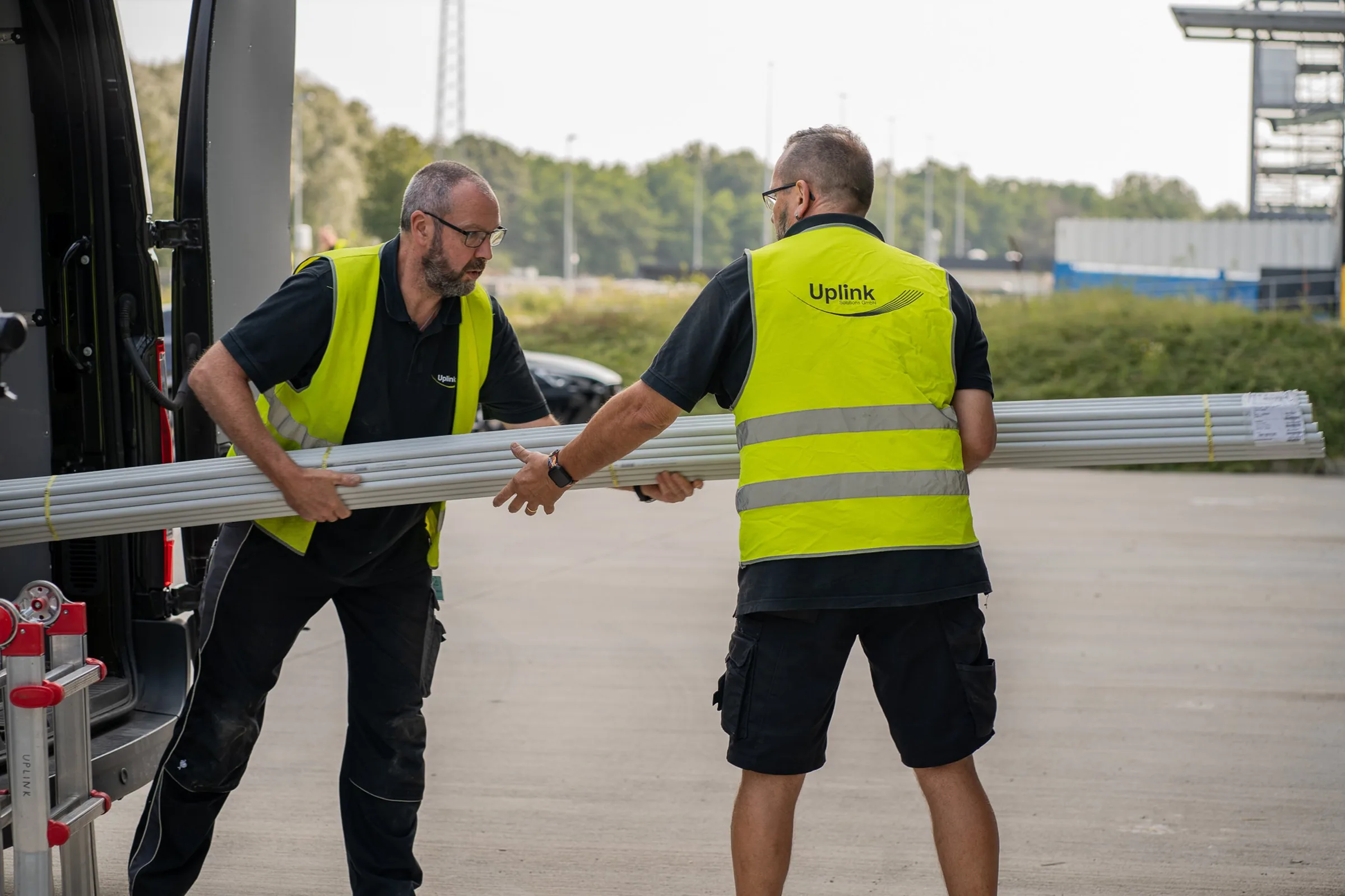 Zwei Techniker in Warnwesten entladen Metallprofile aus einem Transporter