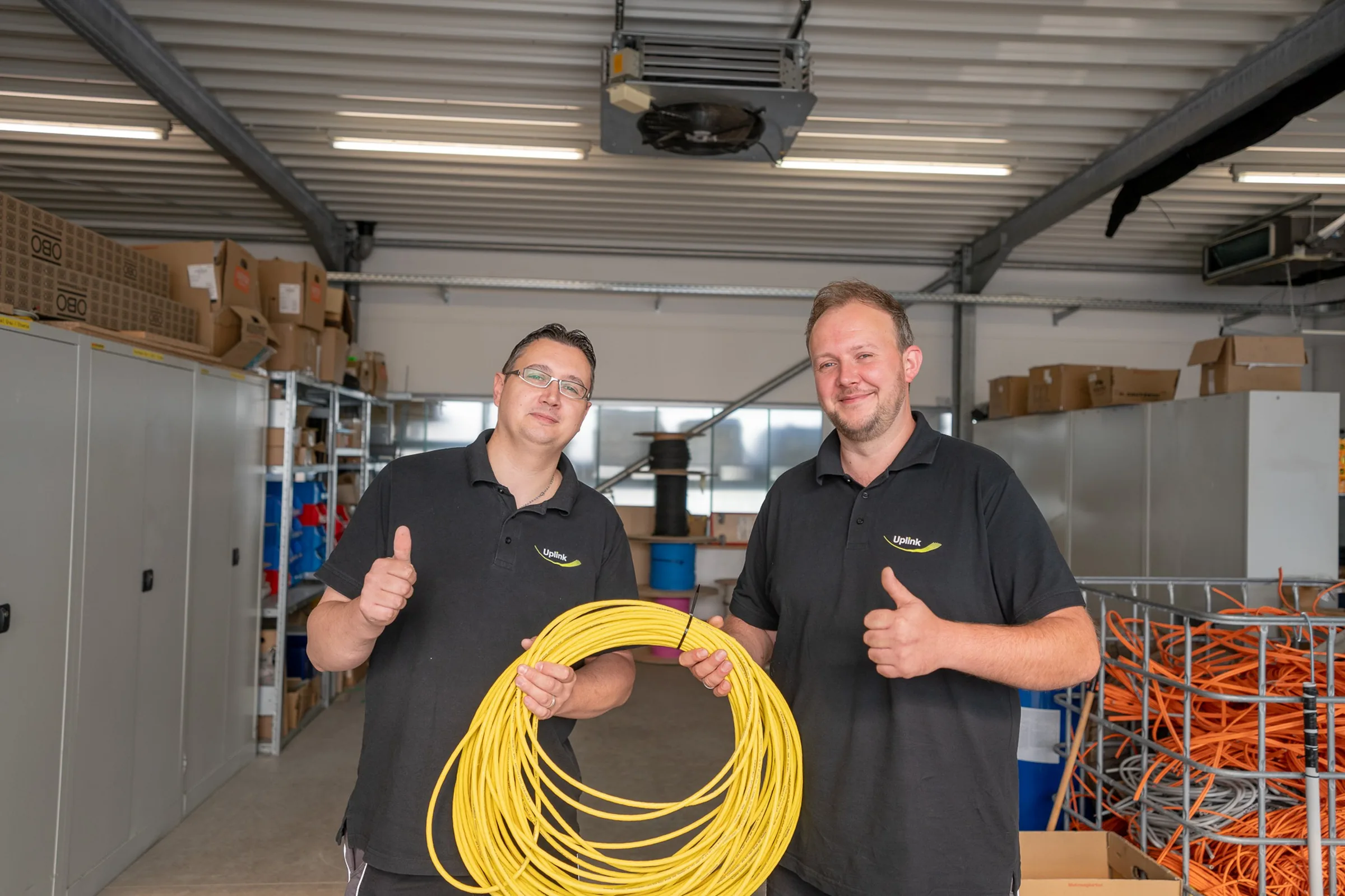 Zwei Uplink-Techniker mit gelbem Glasfaserkabel im Lager