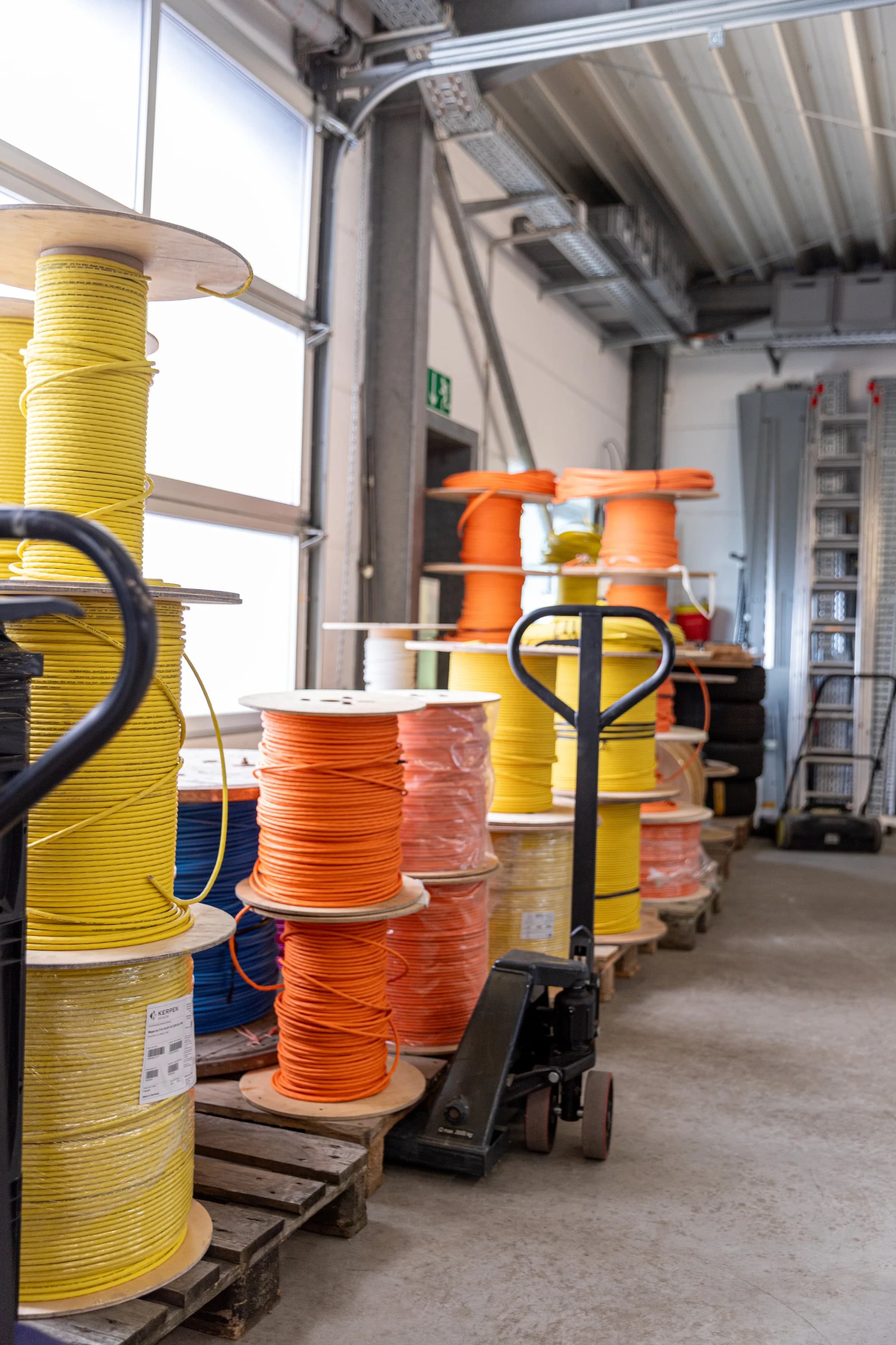 Gelbe und orangefarbene Kabelrollen auf Paletten in einer Lagerhalle