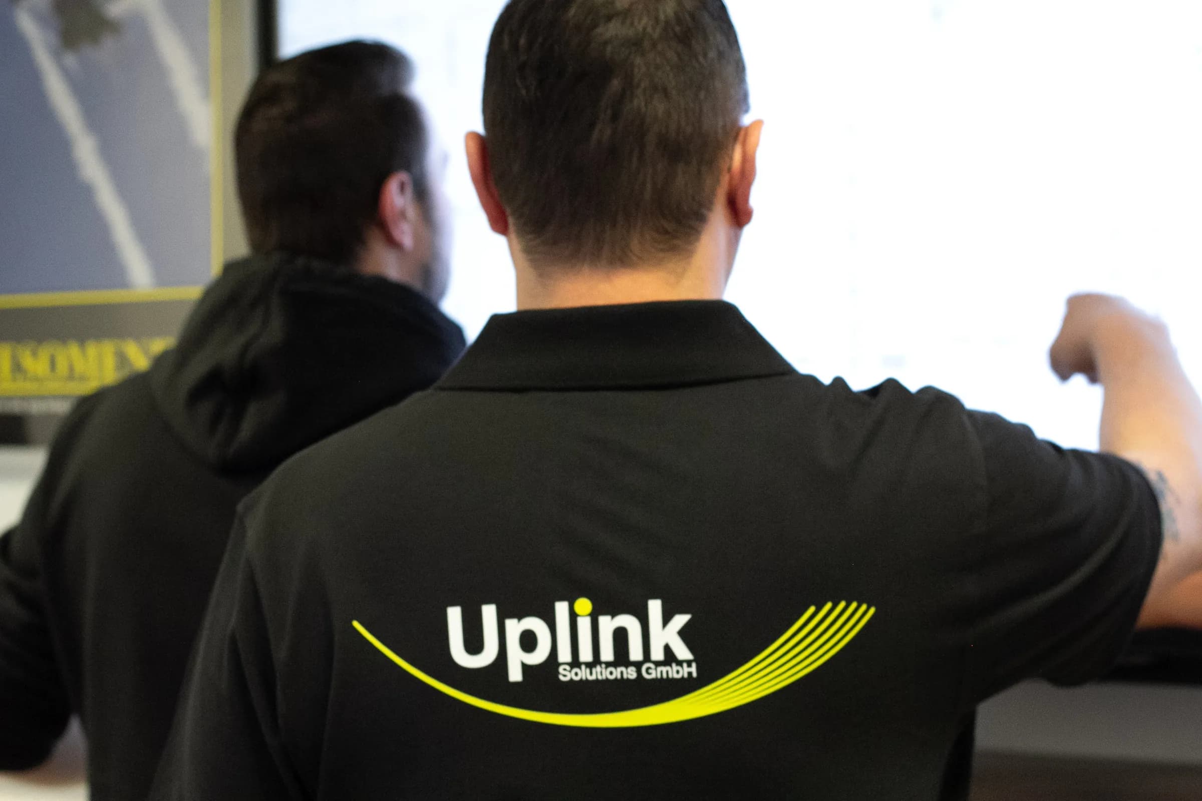 Zwei Uplink-Mitarbeiter von hinten bei der Projektabstimmung vor einem Bildschirm